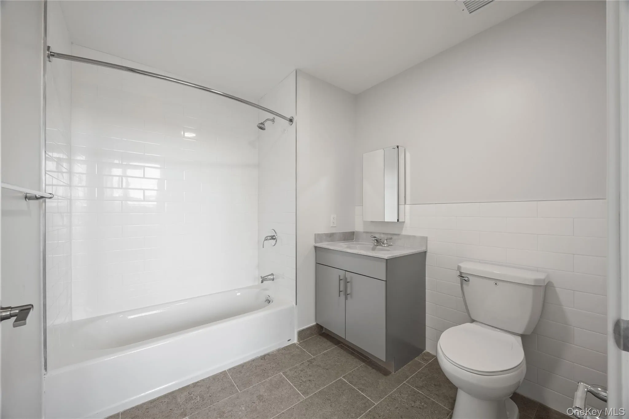 Bathroom featuring shower / bathtub combination, vanity, tile walls, a wainscoted wall, and dark tile patterned flooring Bathroom featuring shower / bathtub combination, vanity, tile walls, a wainscoted wall, and dark tile patterned flooring