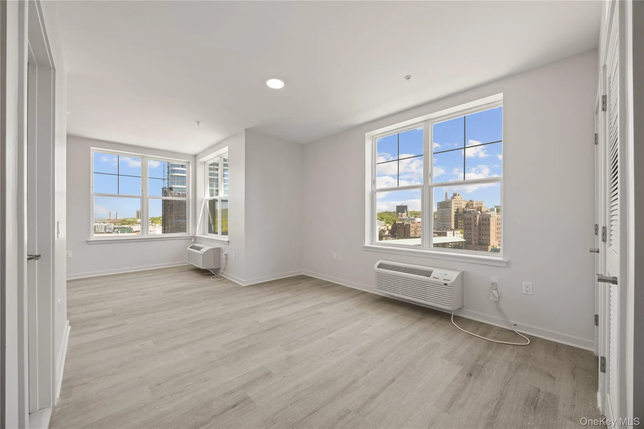 Unfurnished bedroom with light wood-type flooring, a city view, a wall mounted air conditioner, and recessed lighting Unfurnished bedroom with light wood-type flooring, a city view, a wall mounted air conditioner, and recessed lighting