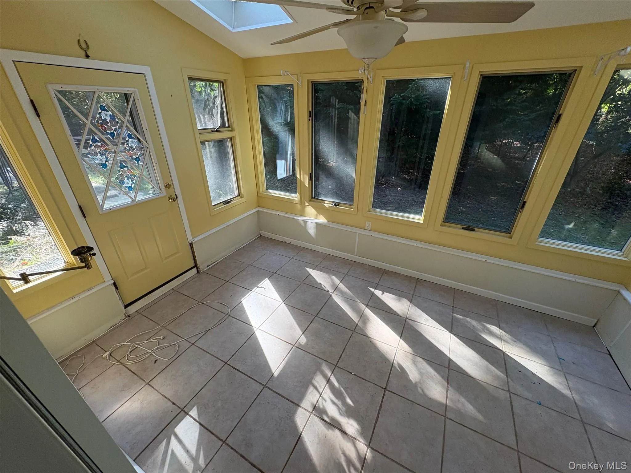 Unfurnished sunroom featuring lofted ceiling, tile patterned floors, and a skylight Unfurnished sunroom featuring lofted ceiling, tile patterned floors, and a skylight