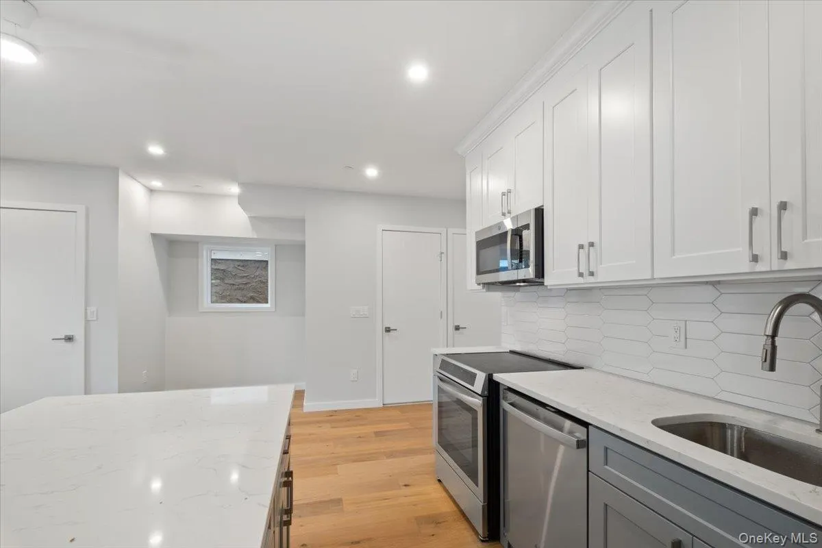 Kitchen featuring appliances with stainless steel finishes, tasteful backsplash, light wood-style floors, light stone counters, and recessed lighting Kitchen featuring appliances with stainless steel finishes, tasteful backsplash, light wood-style floors, light stone counters, and recessed lighting