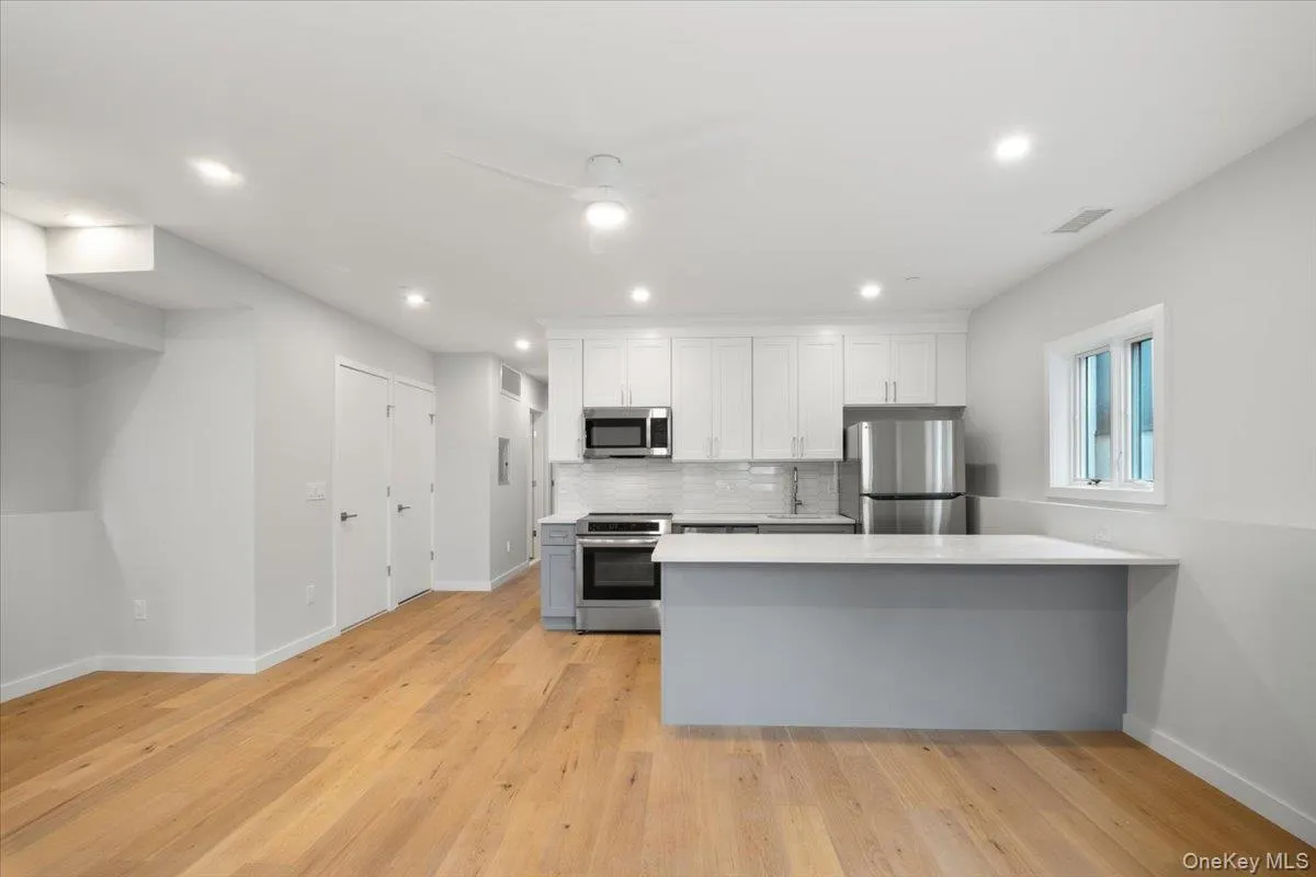 Kitchen featuring stainless steel appliances, white cabinetry, a peninsula, tasteful backsplash, and light wood finished floors Kitchen featuring stainless steel appliances, white cabinetry, a peninsula, tasteful backsplash, and light wood finished floors