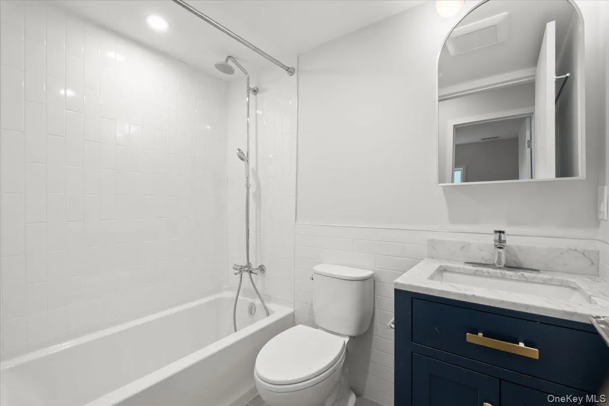 Bathroom featuring vanity, bathing tub / shower combination, wainscoting, recessed lighting, and tile walls Bathroom featuring vanity, bathing tub / shower combination, wainscoting, recessed lighting, and tile walls
