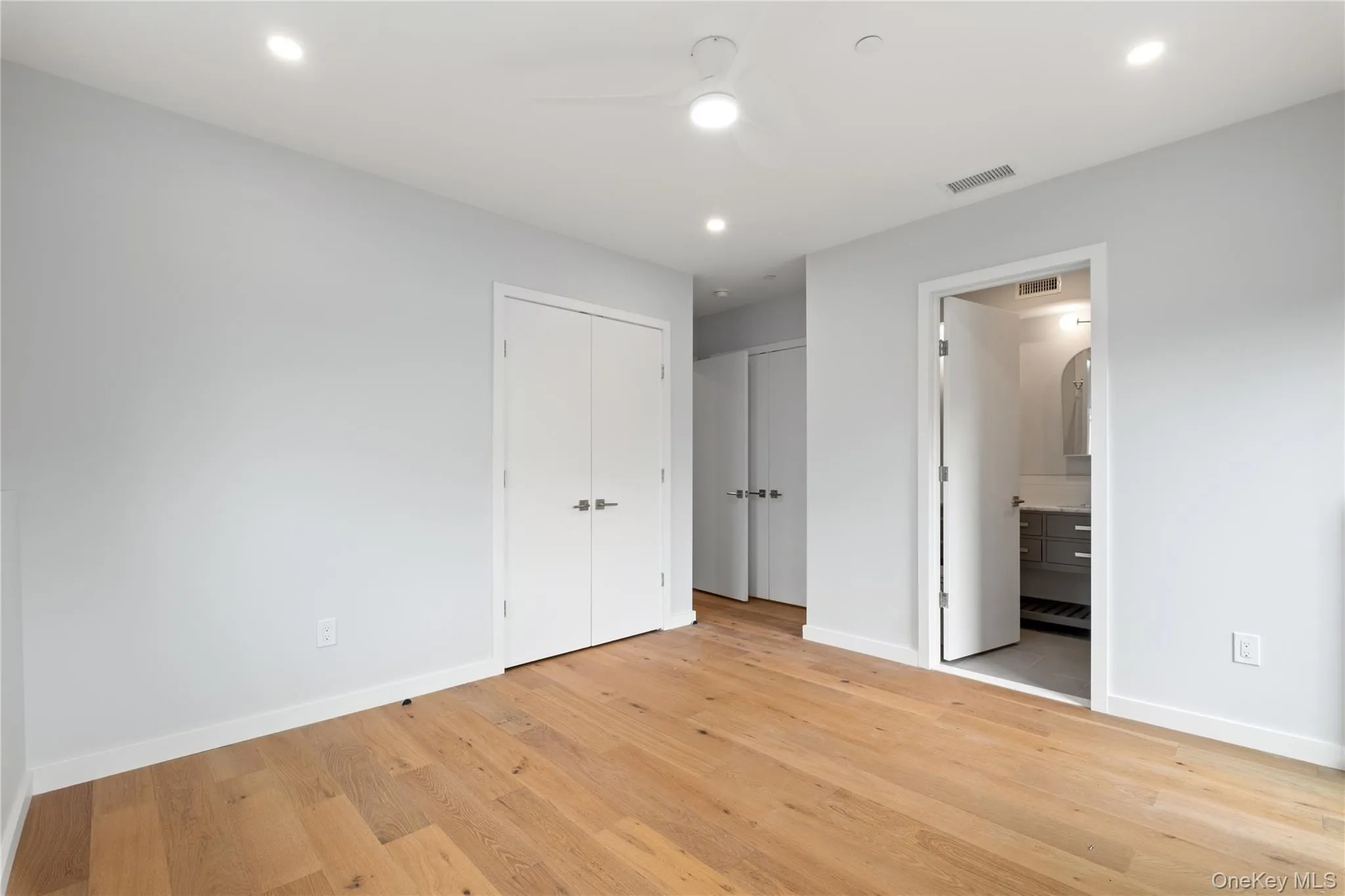 Unfurnished bedroom with recessed lighting, light wood finished floors, ceiling fan, ensuite bath, and two closets Unfurnished bedroom with recessed lighting, light wood finished floors, ceiling fan, ensuite bath, and two closets