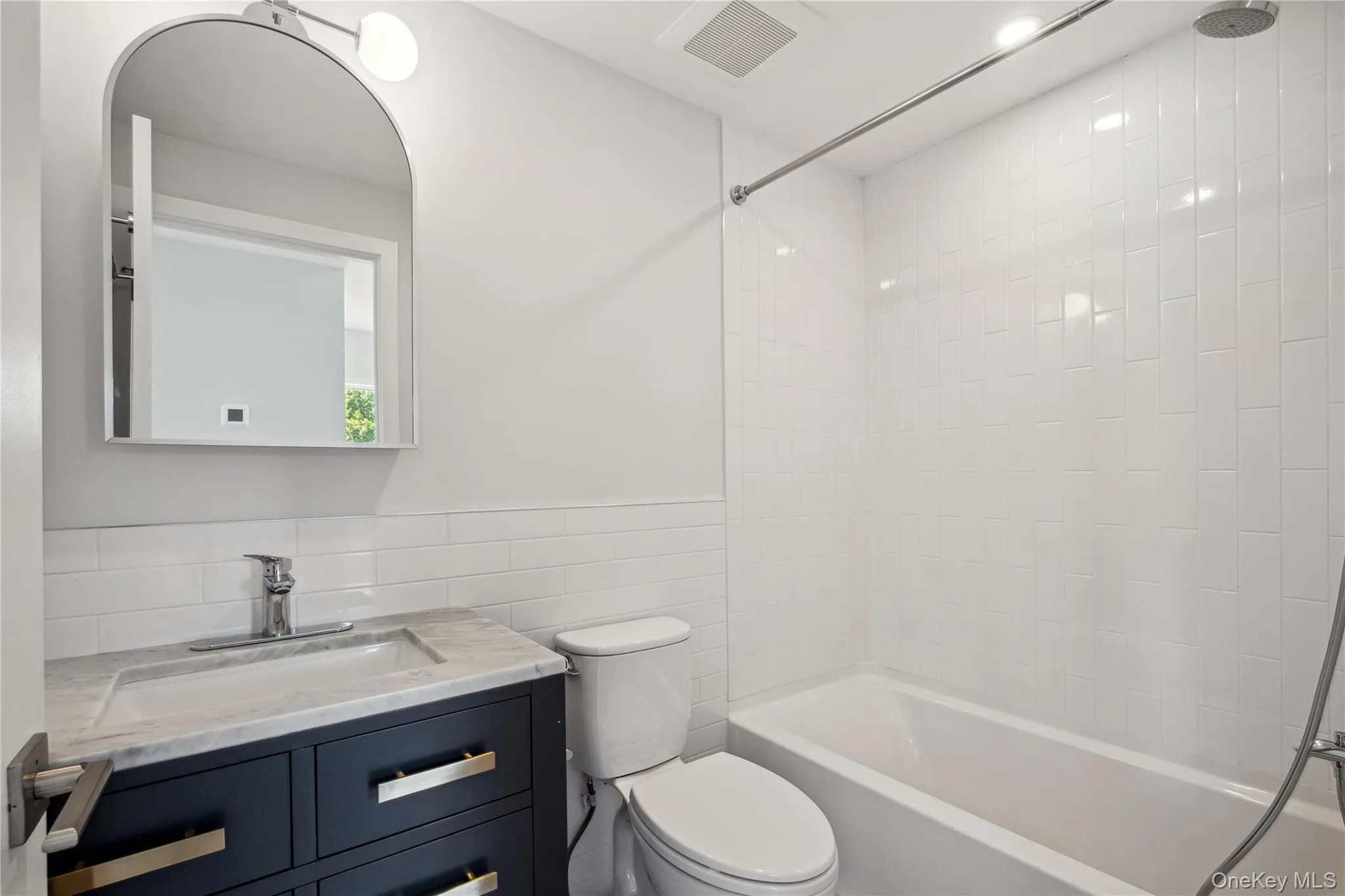 Bathroom with tile walls, vanity, bathtub / shower combination, and wainscoting Bathroom with tile walls, vanity, bathtub / shower combination, and wainscoting