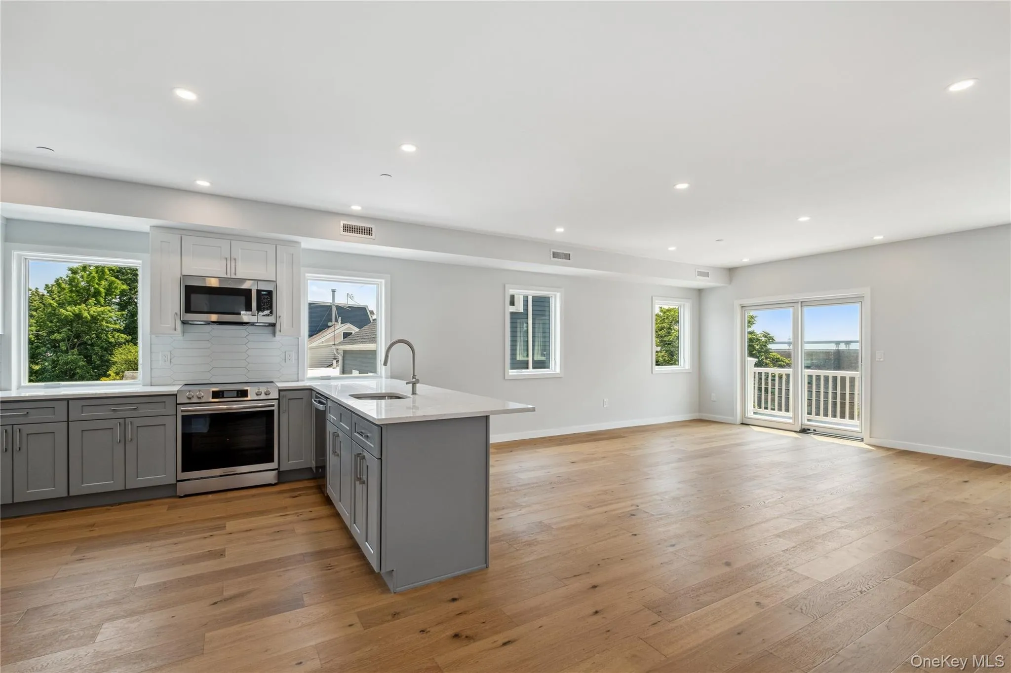 Kitchen with appliances with stainless steel finishes, gray cabinetry, a peninsula, recessed lighting, and light wood-type flooring Kitchen with appliances with stainless steel finishes, gray cabinetry, a peninsula, recessed lighting, and light wood-type flooring