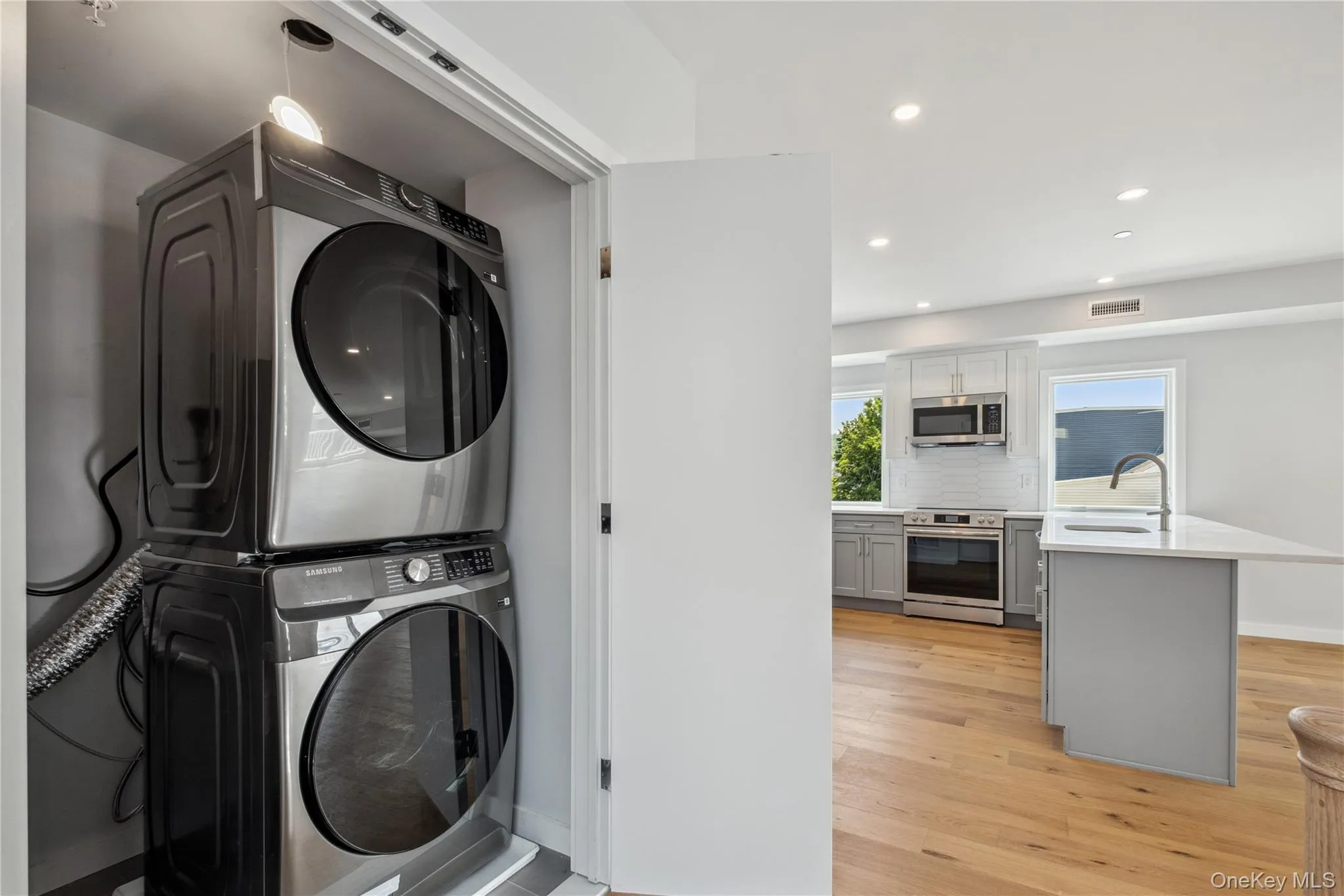 Washroom featuring stacked washing machine and dryer, light wood finished floors, and recessed lighting Washroom featuring stacked washing machine and dryer, light wood finished floors, and recessed lighting