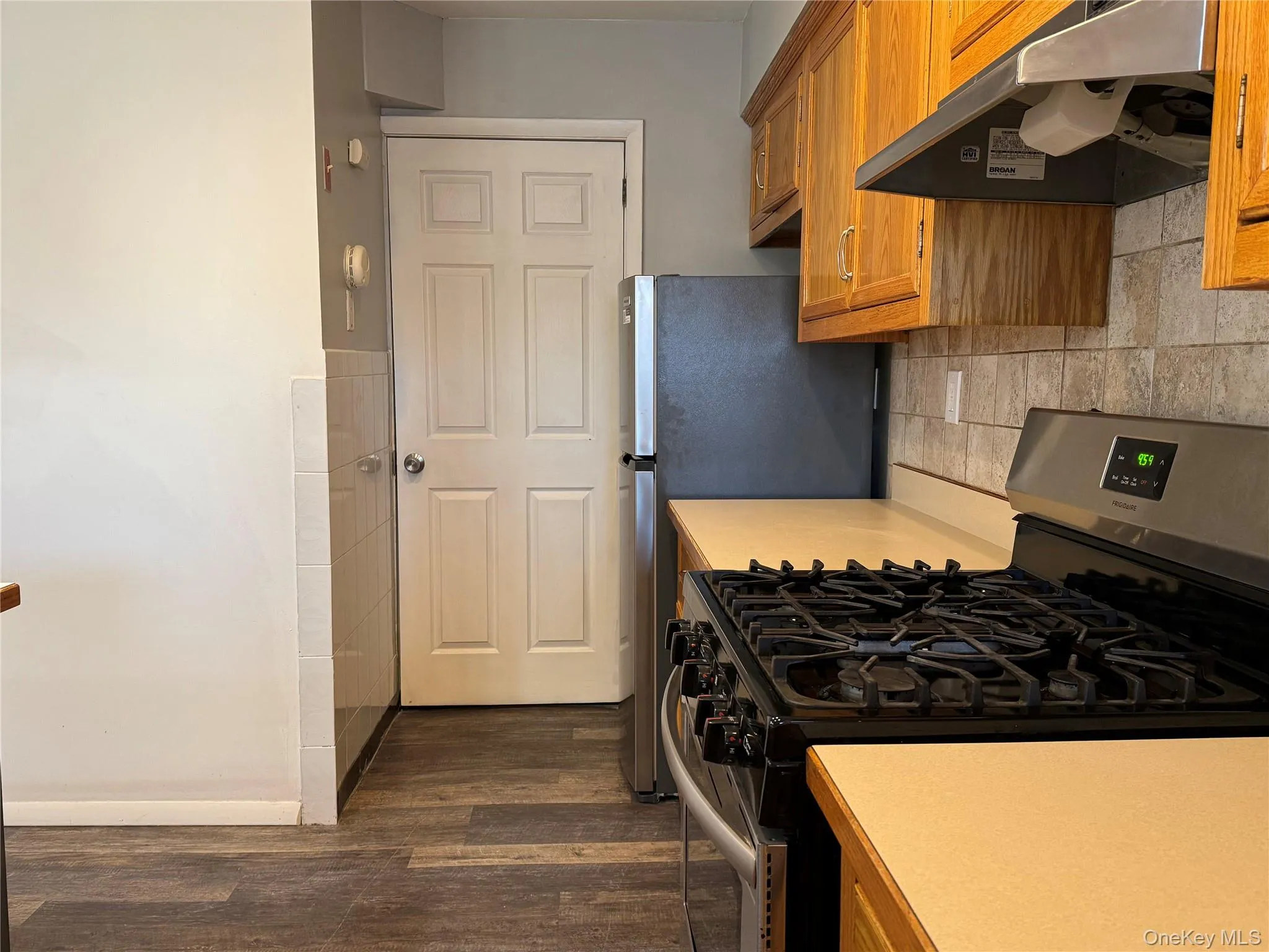 Kitchen featuring dark hardwood / wood-style floors, decorative backsplash, extractor fan, and stainless steel gas range Kitchen featuring dark hardwood / wood-style floors, decorative backsplash, extractor fan, and stainless steel gas range