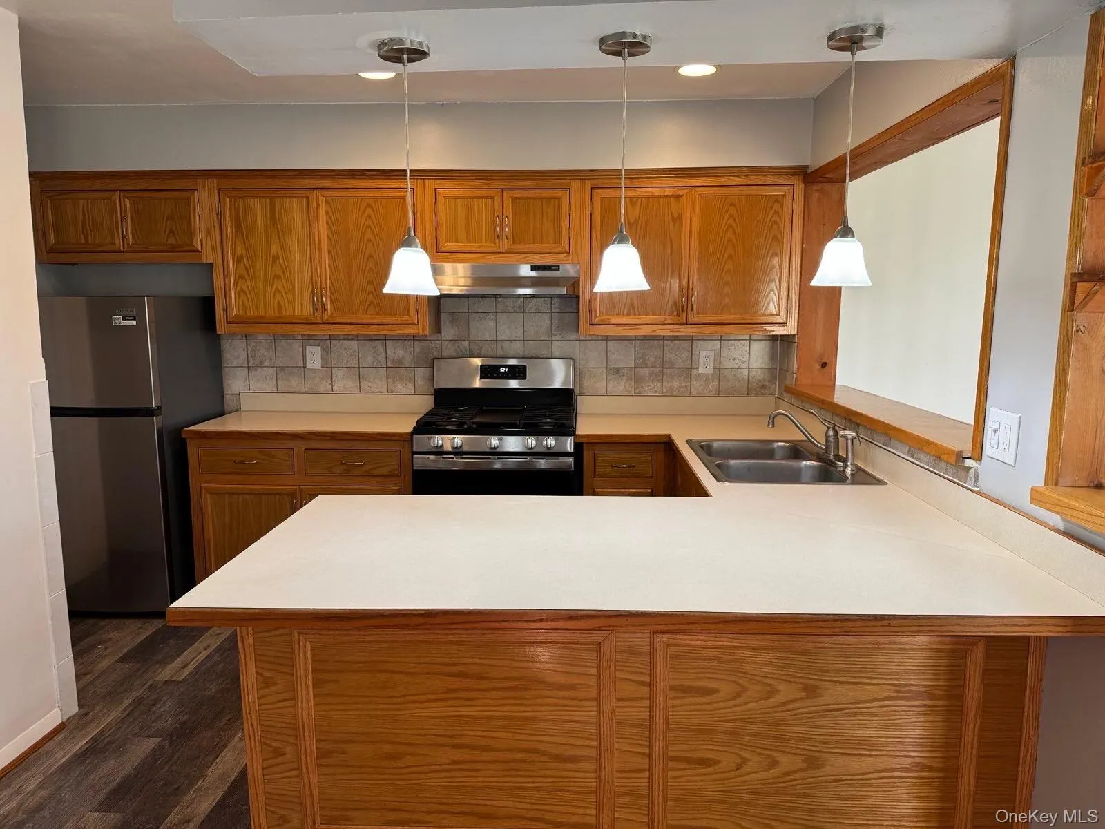 Kitchen featuring brown cabinets, light countertops, appliances with stainless steel finishes, backsplash, and a peninsula Kitchen featuring brown cabinets, light countertops, appliances with stainless steel finishes, backsplash, and a peninsula