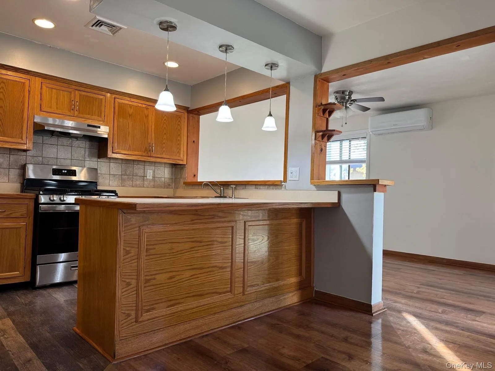 Kitchen with gas stove, brown cabinets, backsplash, pendant lighting, and a peninsula Kitchen with gas stove, brown cabinets, backsplash, pendant lighting, and a peninsula