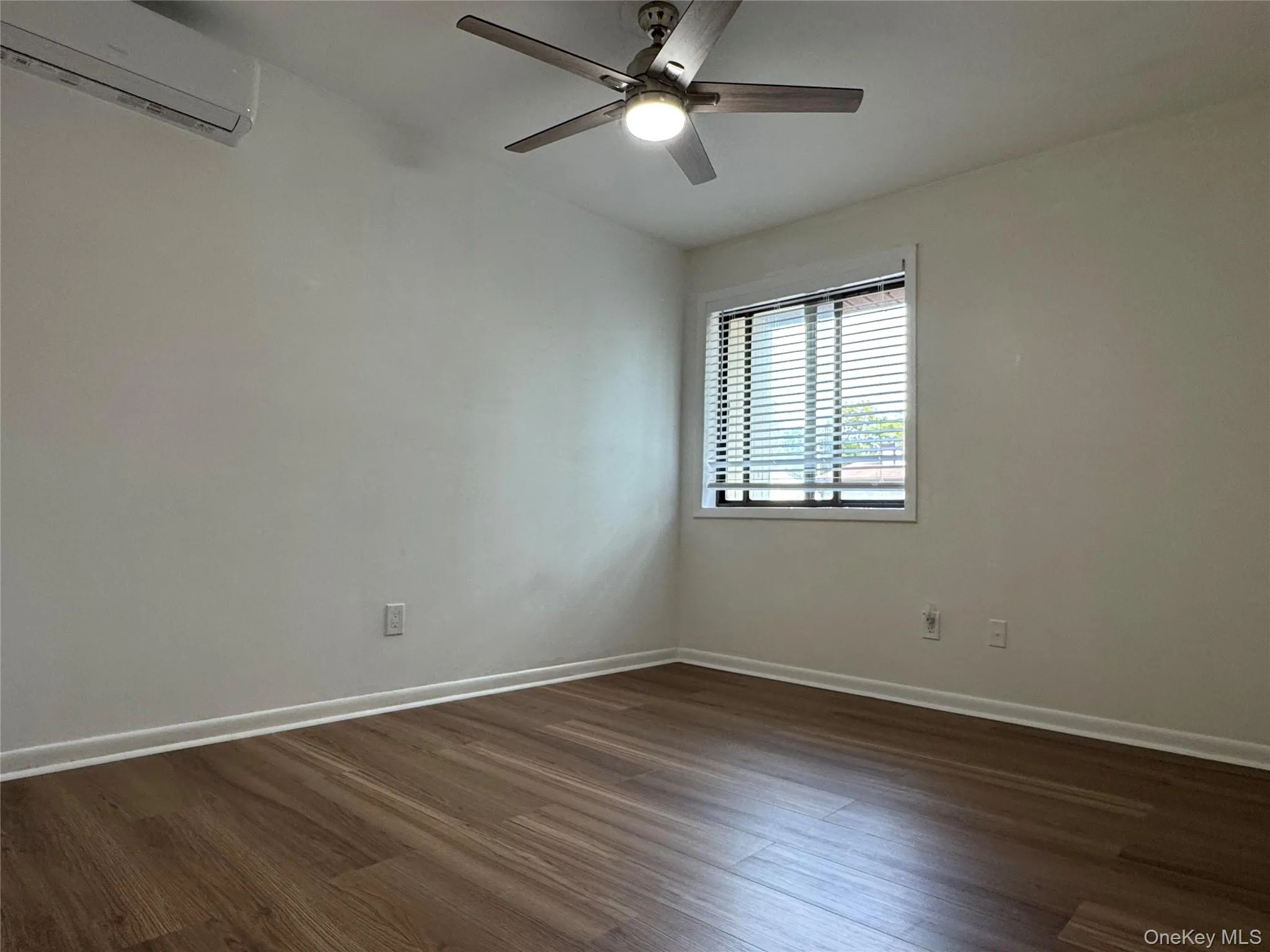 Empty room with dark wood-style flooring, a wall mounted AC, and ceiling fan Empty room with dark wood-style flooring, a wall mounted AC, and ceiling fan