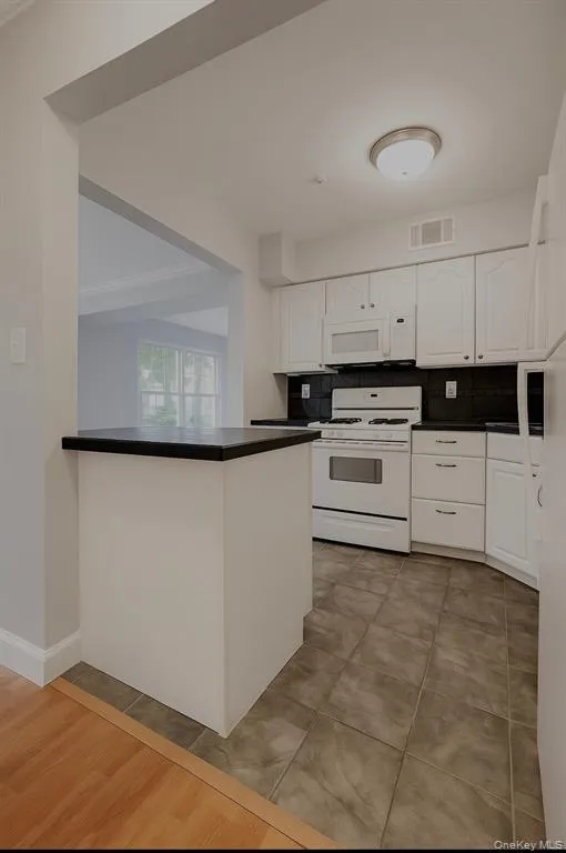 Kitchen featuring backsplash, dark countertops, white appliances, and white cabinetry Kitchen featuring backsplash, dark countertops, white appliances, and white cabinetry