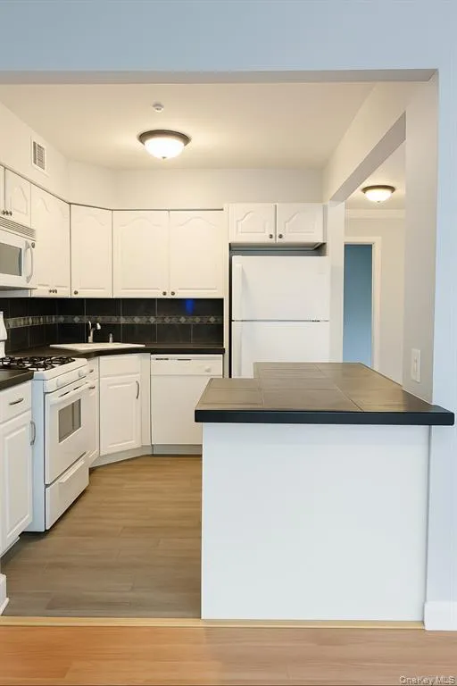 Kitchen with white appliances, white cabinetry, backsplash, and light wood finished floors Kitchen with white appliances, white cabinetry, backsplash, and light wood finished floors