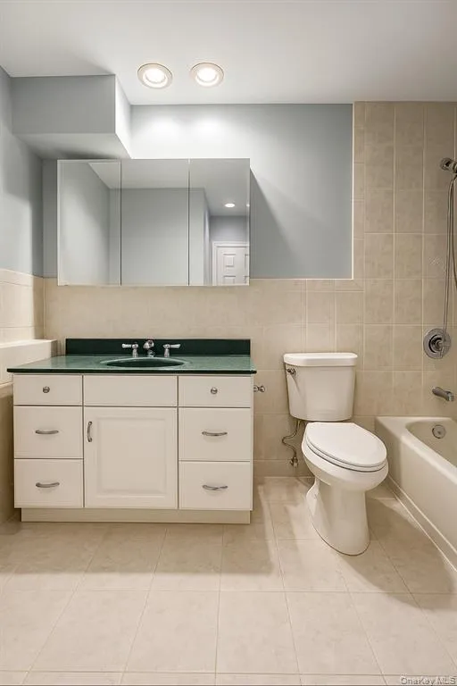Bathroom with tile walls, tub / shower combination, vanity, light tile patterned floors, and recessed lighting Bathroom with tile walls, tub / shower combination, vanity, light tile patterned floors, and recessed lighting