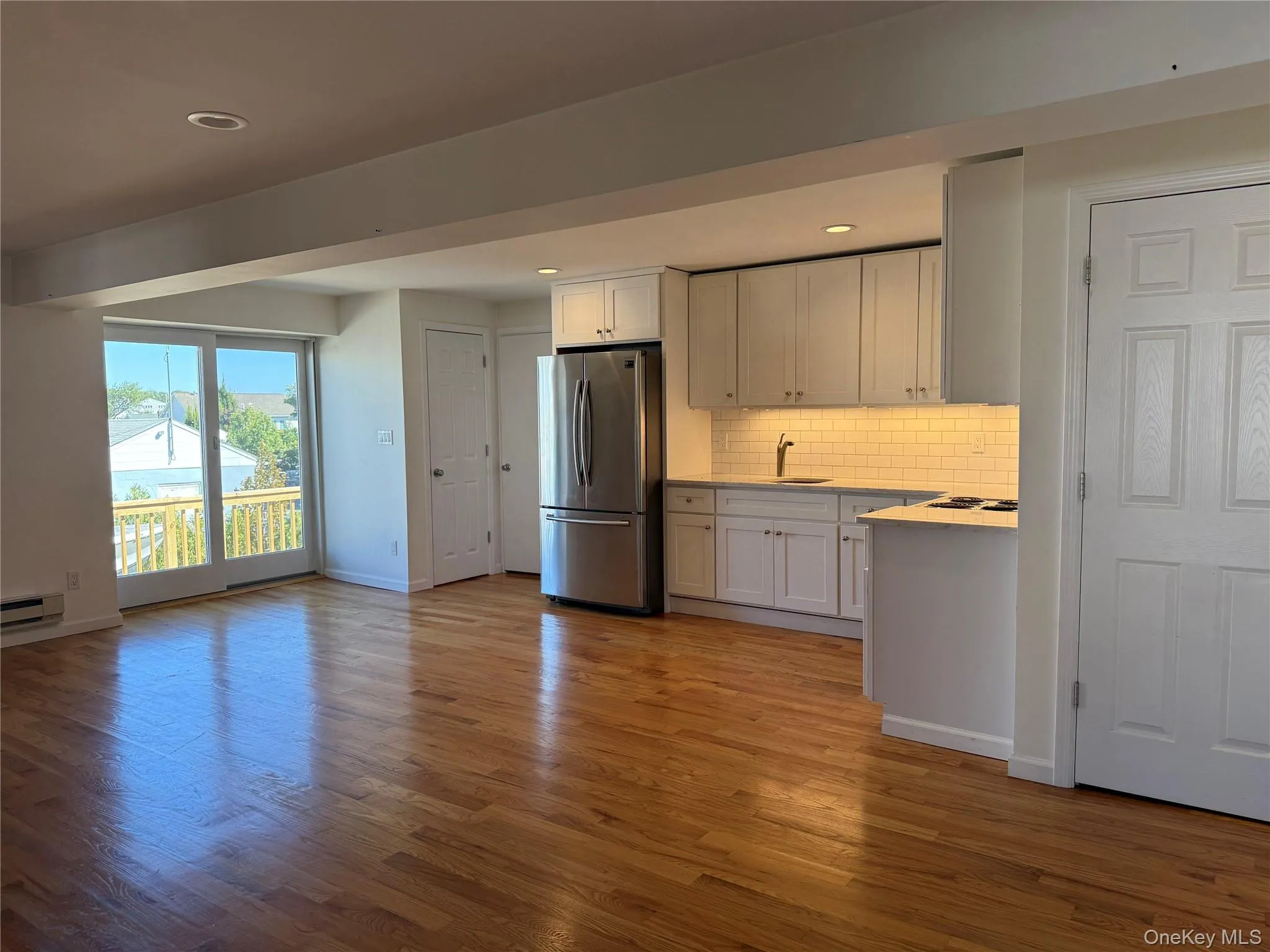 Kitchen/living room with wood finished floors, freestanding refrigerator, tasteful backsplash, white cabinets, and recessed lighting Kitchen/living room with wood finished floors, freestanding refrigerator, tasteful backsplash, white cabinets, and recessed lighting