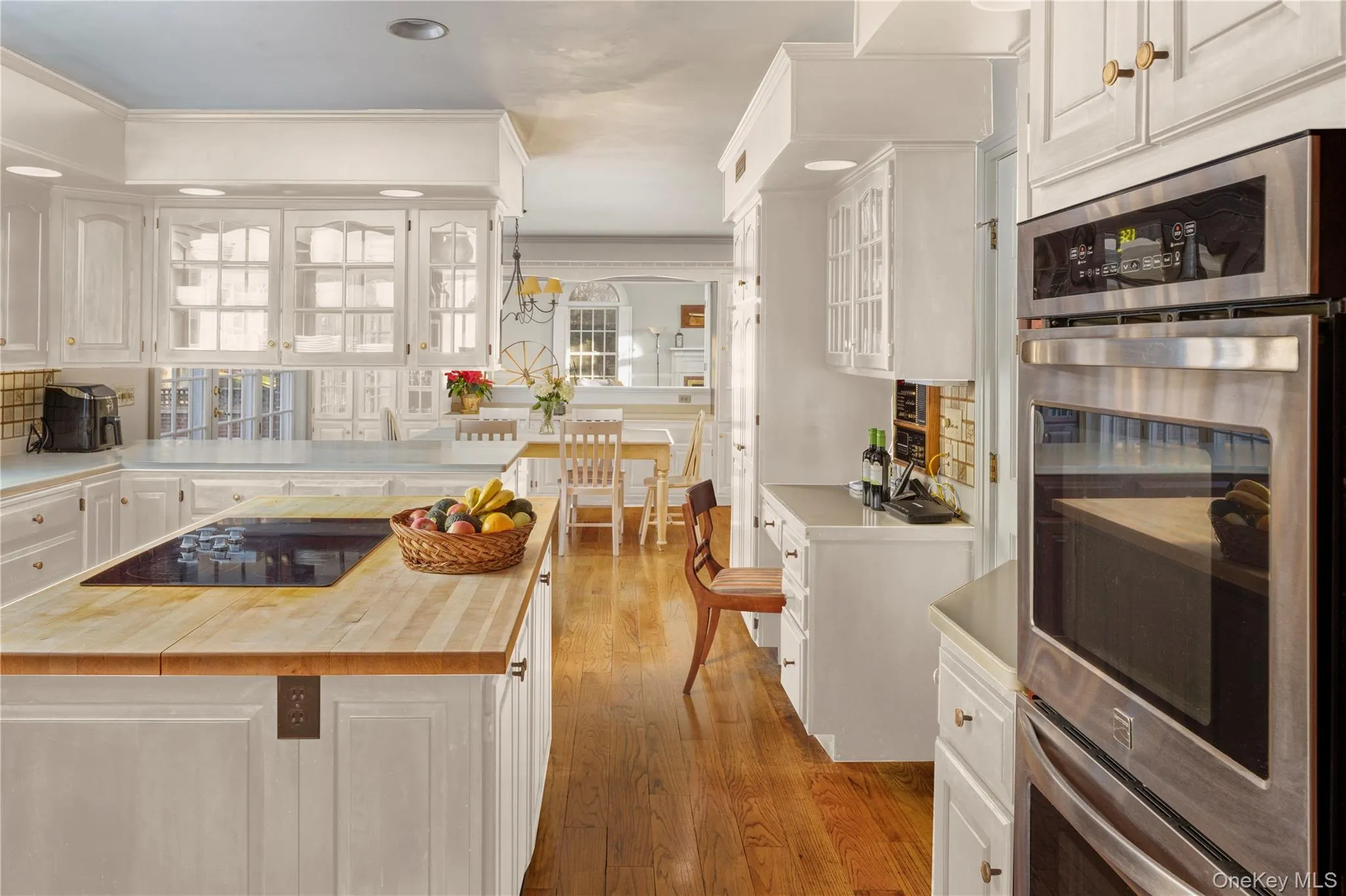 Kitchen with white cabinets, black electric cooktop, oven, light wood-type flooring, and butcher block countertops Kitchen with white cabinets, black electric cooktop, oven, light wood-type flooring, and butcher block countertops