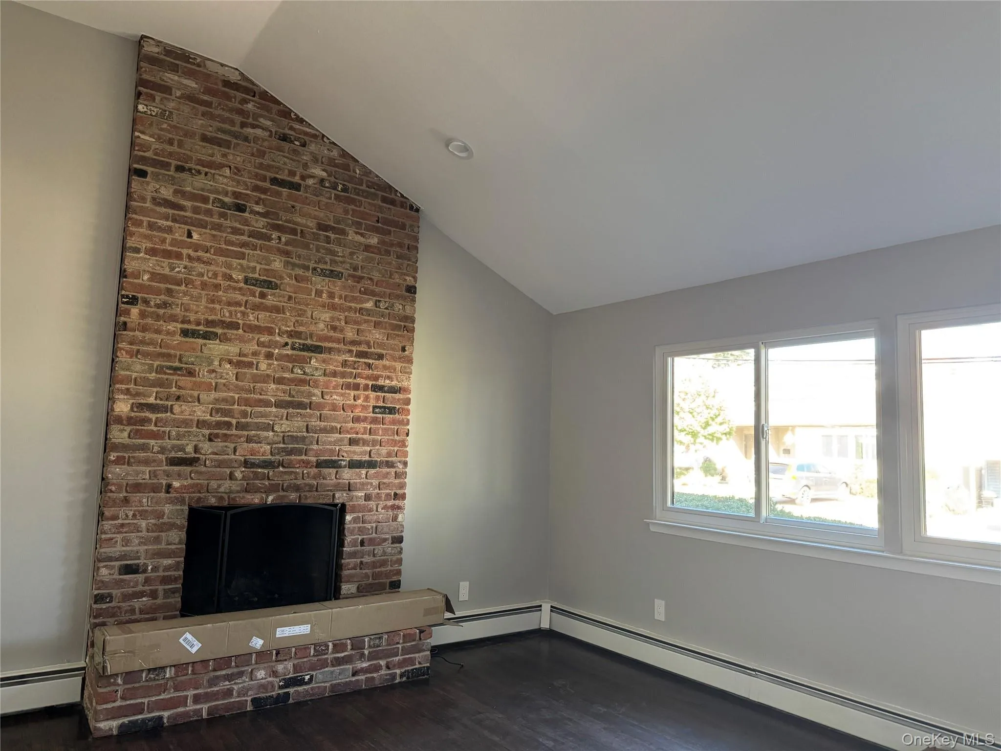 Unfurnished living room with a fireplace, vaulted ceiling, a baseboard heating unit, and dark wood-type flooring Unfurnished living room with a fireplace, vaulted ceiling, a baseboard heating unit, and dark wood-type flooring