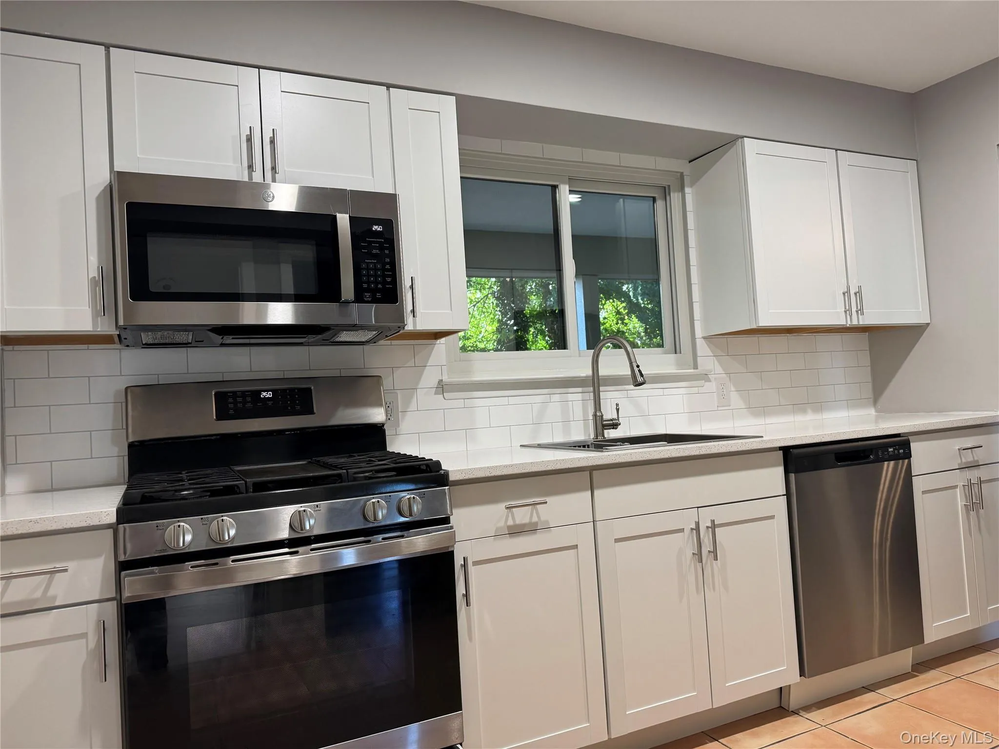 Kitchen featuring appliances with stainless steel finishes, white cabinets, backsplash, light tile patterned flooring, and light stone counters Kitchen featuring appliances with stainless steel finishes, white cabinets, backsplash, light tile patterned flooring, and light stone counters