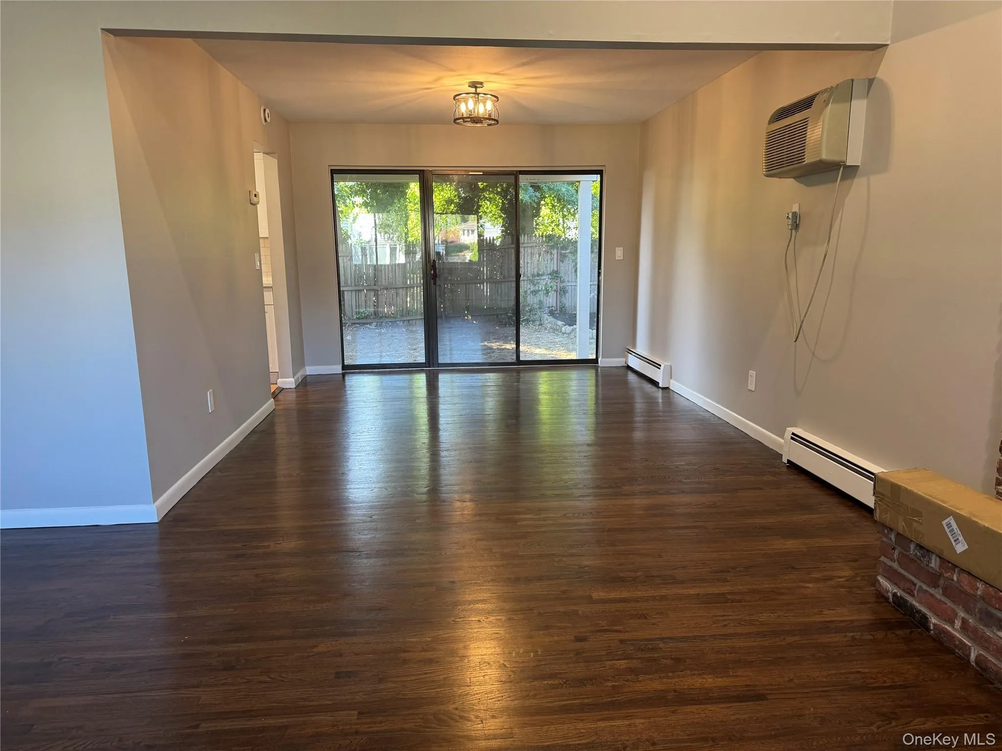 Dining Rm with sliders to rear patio. Dark wood-type flooring, a baseboard heating unit, and a wall mounted AC Dining Rm with sliders to rear patio. Dark wood-type flooring, a baseboard heating unit, and a wall mounted AC