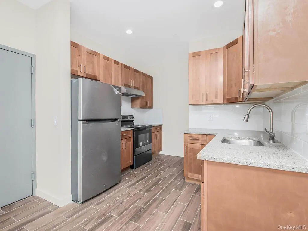 Kitchen with appliances with stainless steel finishes, light stone countertops, tasteful backsplash, wood tiled floors, and under cabinet range hood Kitchen with appliances with stainless steel finishes, light stone countertops, tasteful backsplash, wood tiled floors, and under cabinet range hood