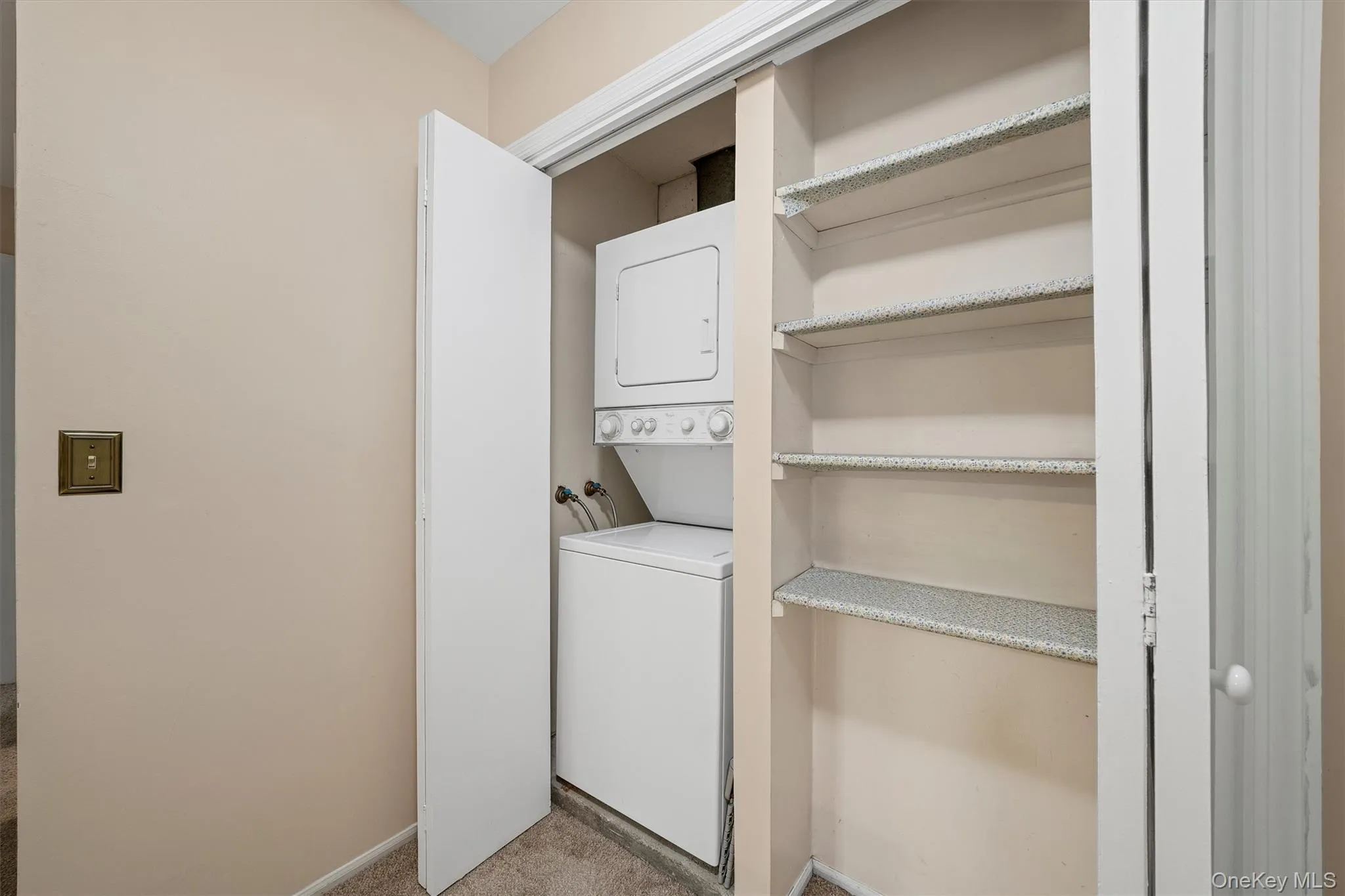 Laundry room featuring estacked washer and dryer and light colored carpet Laundry room featuring estacked washer and dryer and light colored carpet