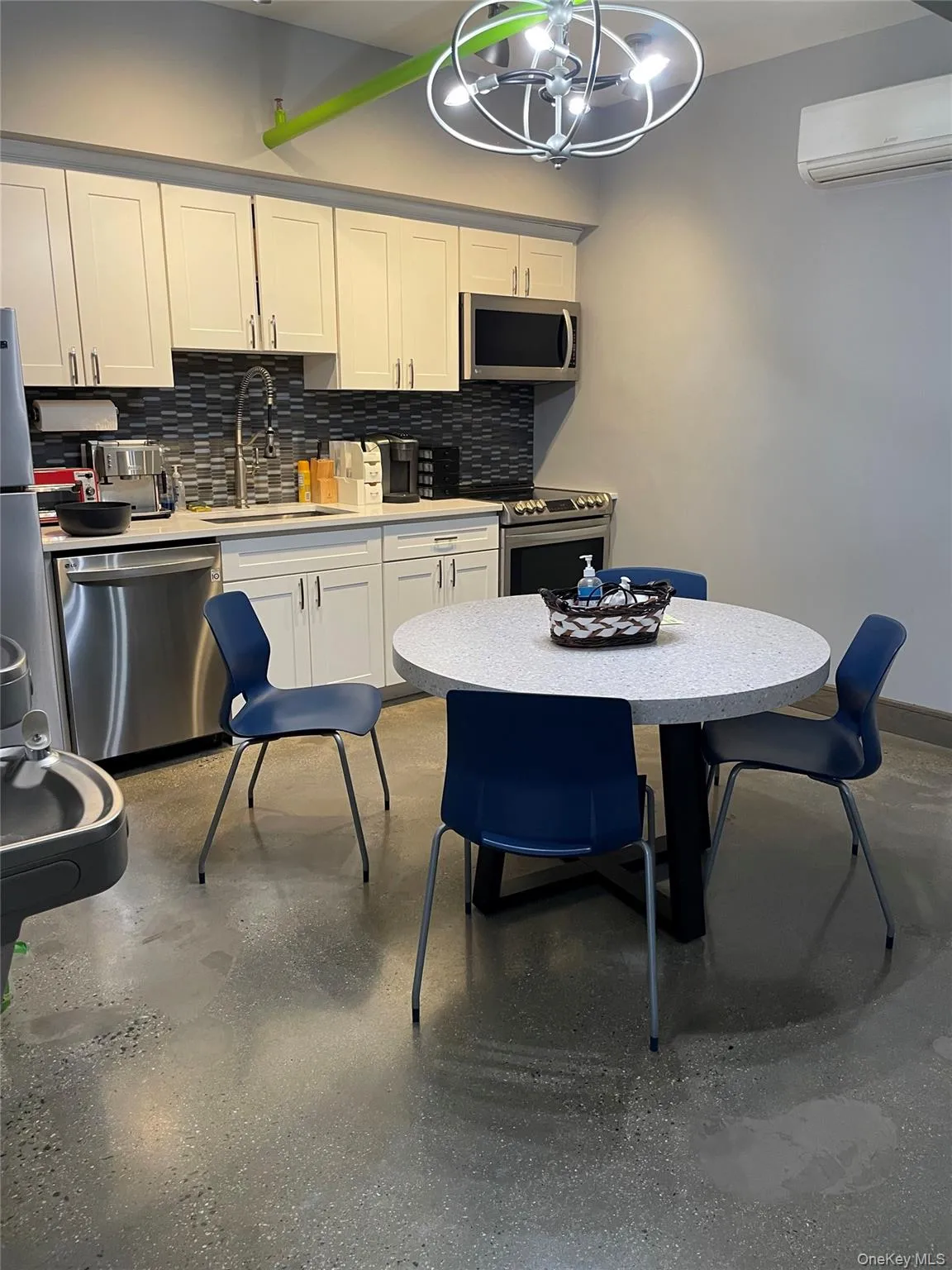 Kitchen with white cabinets, appliances with stainless steel finishes, light countertops, decorative backsplash, and a wall unit AC Kitchen with white cabinets, appliances with stainless steel finishes, light countertops, decorative backsplash, and a wall unit AC