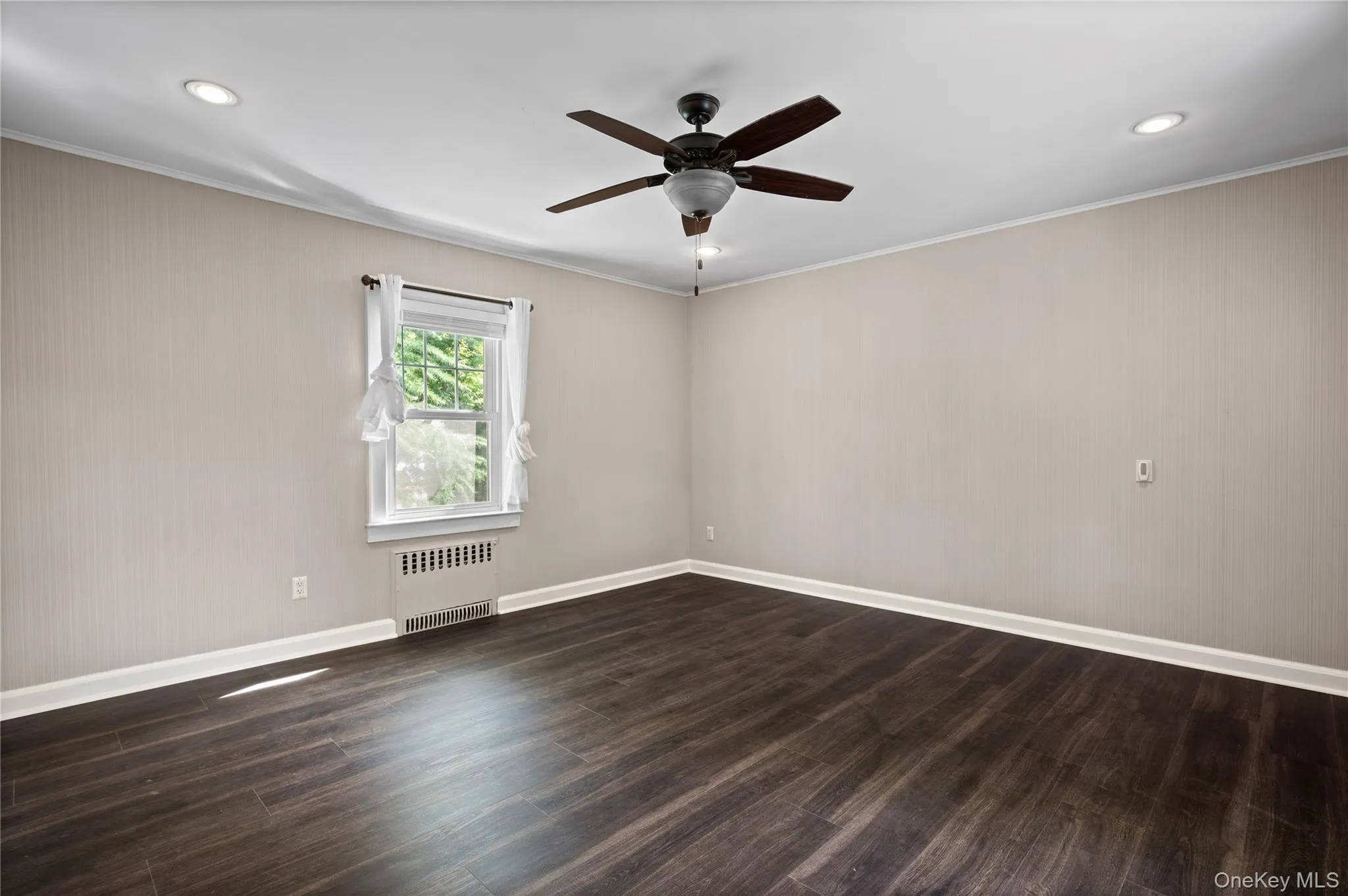 Empty room with ornamental molding, dark wood finished floors, radiator heating unit, ceiling fan, and recessed lighting Empty room with ornamental molding, dark wood finished floors, radiator heating unit, ceiling fan, and recessed lighting