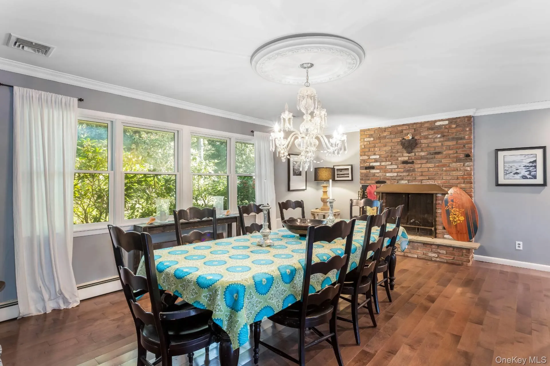 Dining room with dark wood finished floors, a brick fireplace, ornamental molding, a chandelier, and a baseboard radiator Dining room with dark wood finished floors, a brick fireplace, ornamental molding, a chandelier, and a baseboard radiator