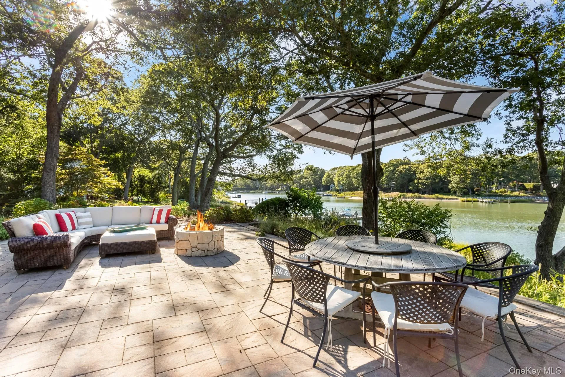 View of patio featuring outdoor dining space, a water view, an outdoor living space with a fire pit, and view of wooded area View of patio featuring outdoor dining space, a water view, an outdoor living space with a fire pit, and view of wooded area