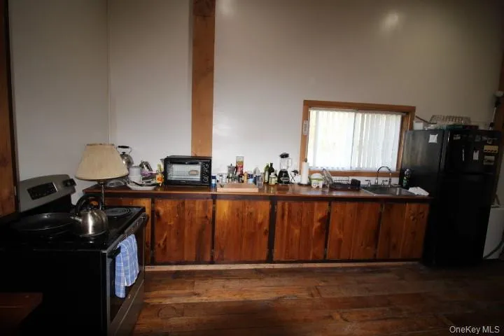 Kitchen with stainless steel electric stove, freestanding refrigerator, dark wood-type flooring, brown cabinets, and dark countertops Kitchen with stainless steel electric stove, freestanding refrigerator, dark wood-type flooring, brown cabinets, and dark countertops