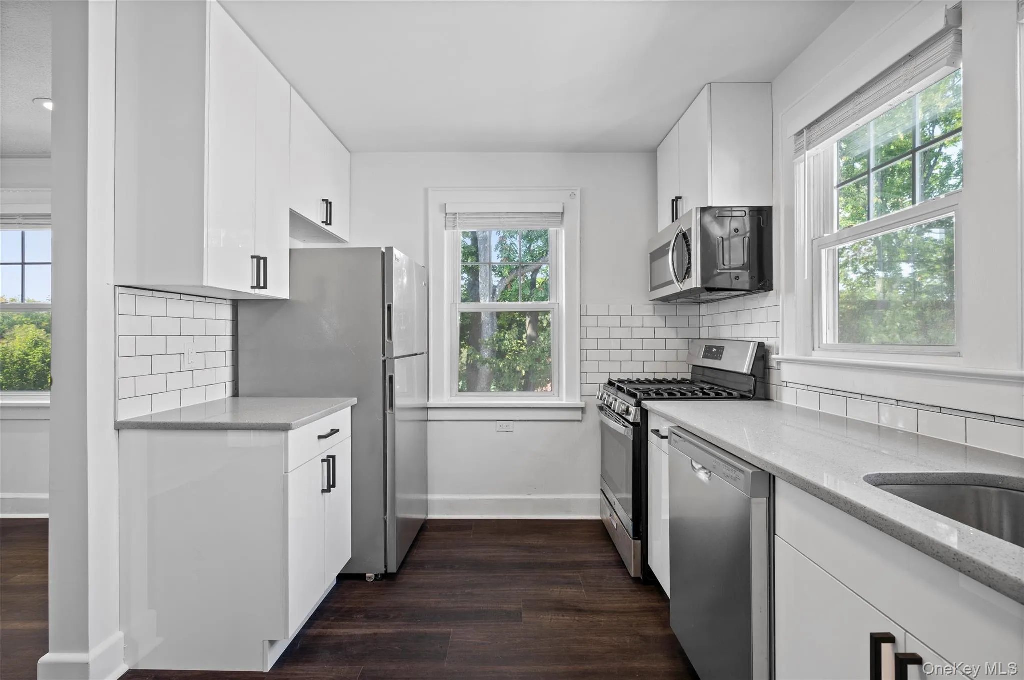 Kitchen with appliances with stainless steel finishes, light stone counters, dark wood-type flooring, and backsplash Kitchen with appliances with stainless steel finishes, light stone counters, dark wood-type flooring, and backsplash