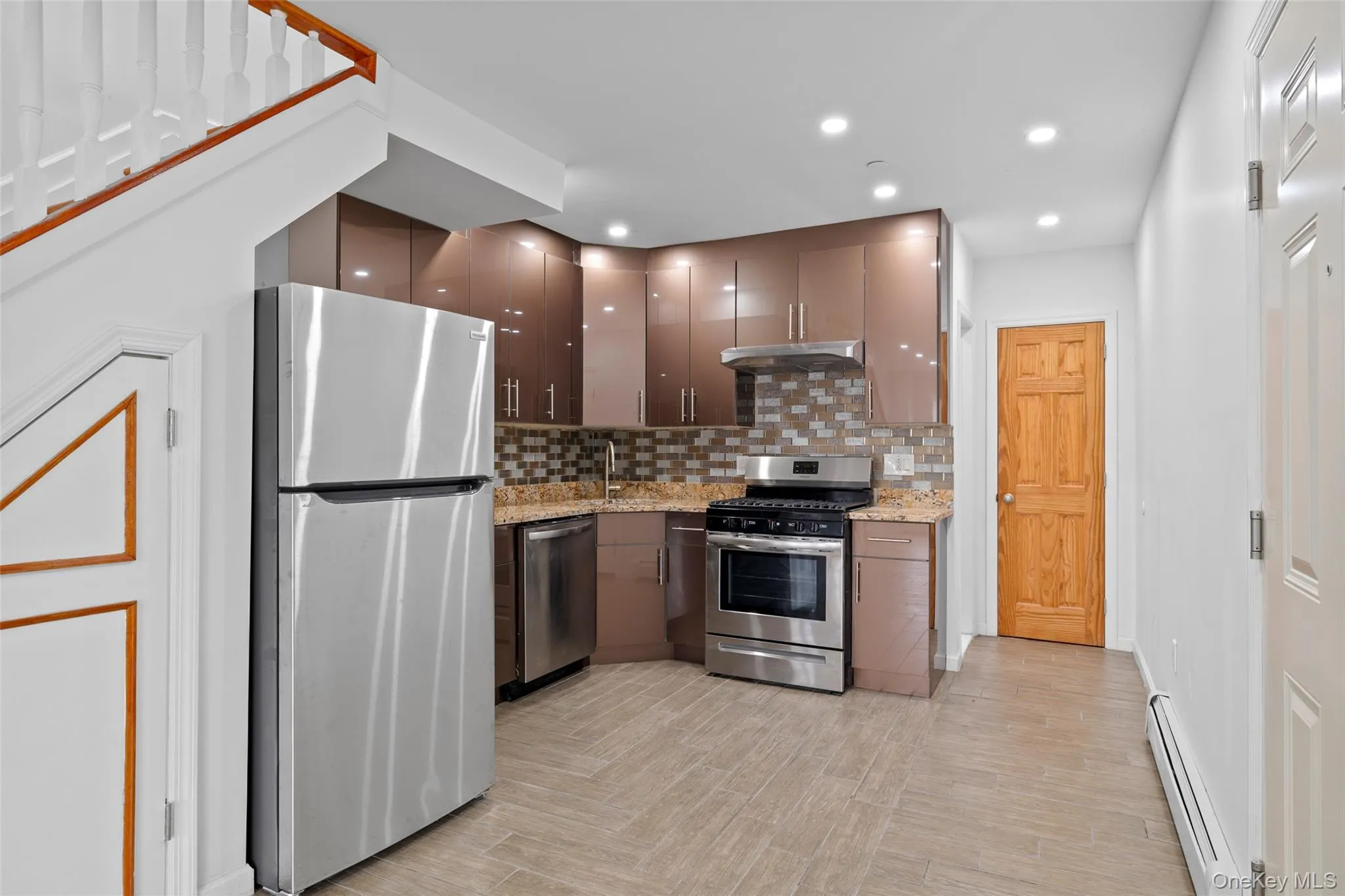 Kitchen with tasteful backsplash, stainless steel appliances, baseboard heating, light stone counters, and recessed lighting Kitchen with tasteful backsplash, stainless steel appliances, baseboard heating, light stone counters, and recessed lighting