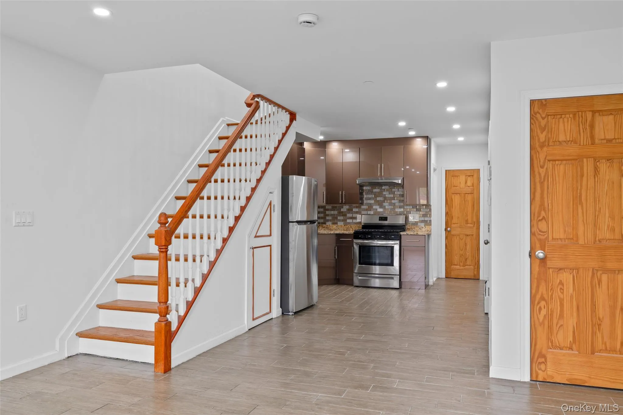 Kitchen with decorative backsplash, recessed lighting, stainless steel appliances, light wood-style flooring, and light stone countertops Kitchen with decorative backsplash, recessed lighting, stainless steel appliances, light wood-style flooring, and light stone countertops