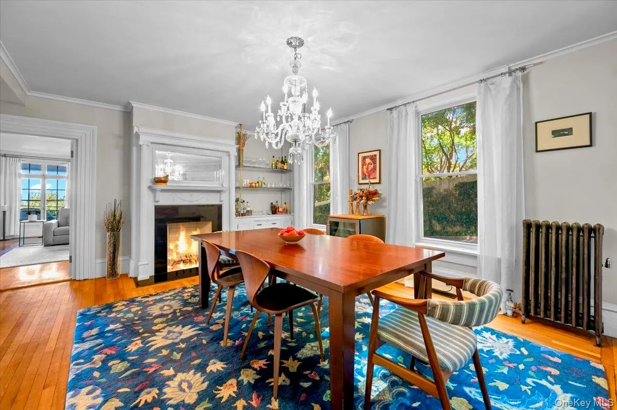 Dining space with light wood-type flooring, radiator, ornamental molding, a high end fireplace, and a chandelier Dining space with light wood-type flooring, radiator, ornamental molding, a high end fireplace, and a chandelier