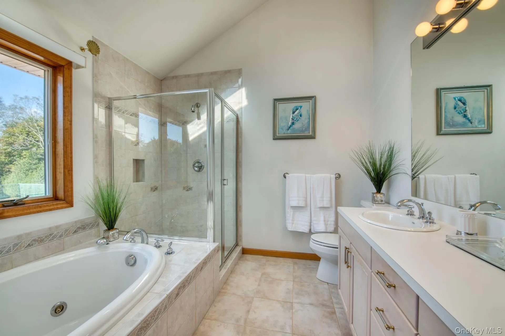 Full bathroom with vaulted ceiling, a bath, vanity, a stall shower, and light tile patterned floors Full bathroom with vaulted ceiling, a bath, vanity, a stall shower, and light tile patterned floors