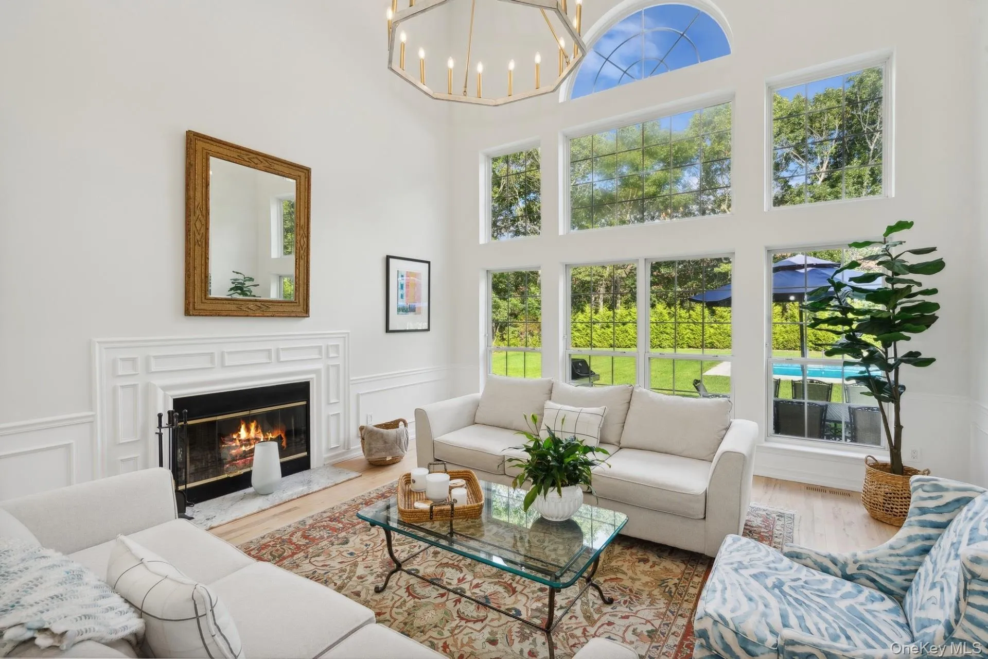 Living area with wood finished floors, a high ceiling, a fireplace, a decorative wall, and a chandelier Living area with wood finished floors, a high ceiling, a fireplace, a decorative wall, and a chandelier