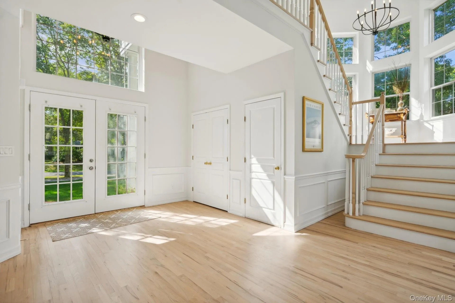 Foyer with a towering ceiling, a decorative wall, stairway, light wood finished floors, and french doors Foyer with a towering ceiling, a decorative wall, stairway, light wood finished floors, and french doors