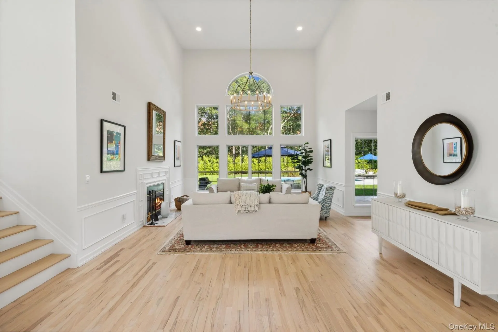 Living room featuring light wood-style floors, wainscoting, a decorative wall, a chandelier, and a lit fireplace Living room featuring light wood-style floors, wainscoting, a decorative wall, a chandelier, and a lit fireplace