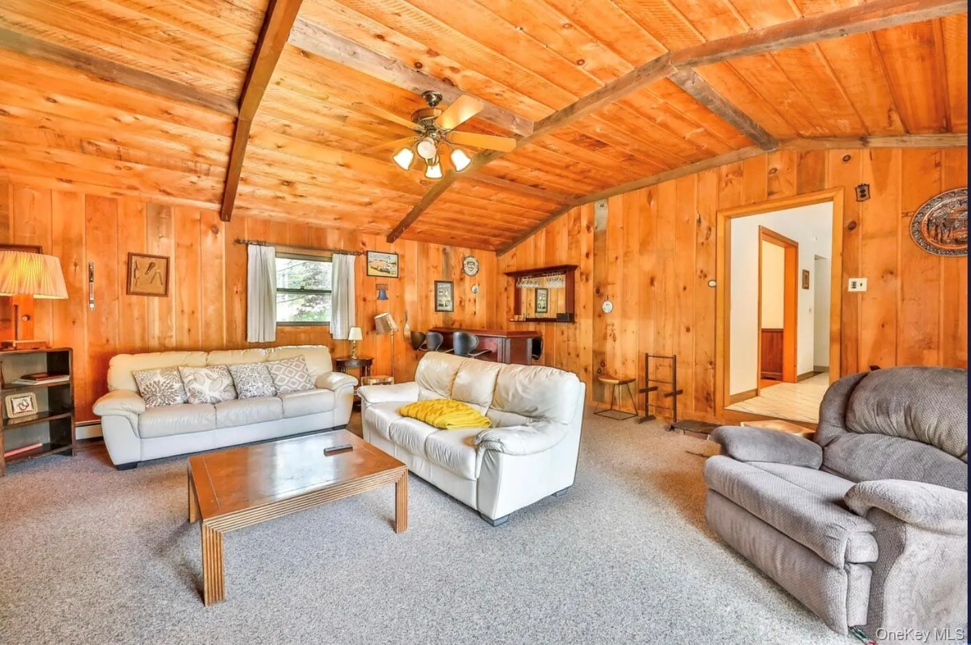Carpeted living room with wooden walls, wood ceiling, and a ceiling fan Carpeted living room with wooden walls, wood ceiling, and a ceiling fan