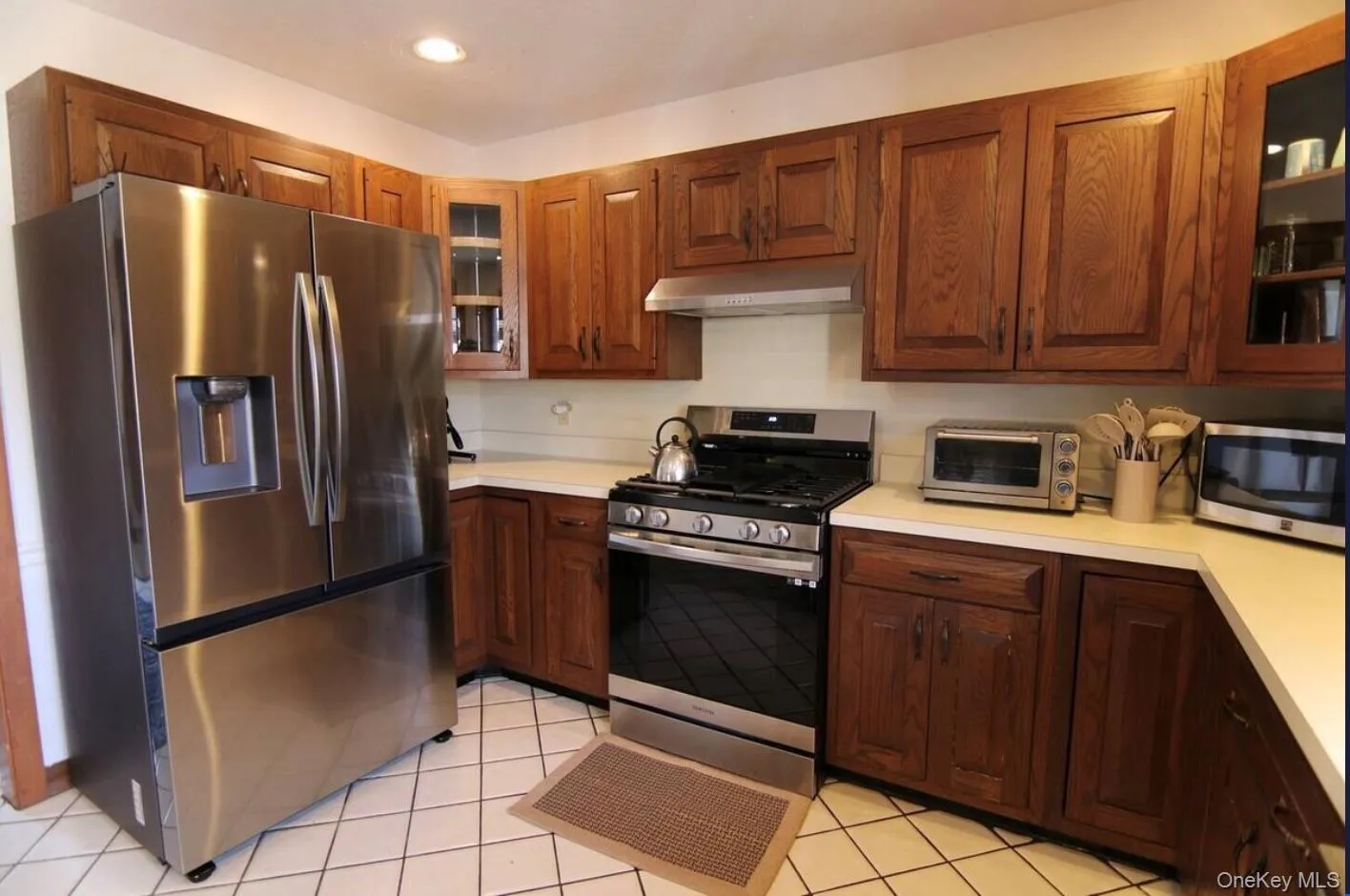 Kitchen featuring glass insert cabinets, appliances with stainless steel finishes, light countertops, light tile patterned floors, and recessed lighting Kitchen featuring glass insert cabinets, appliances with stainless steel finishes, light countertops, light tile patterned floors, and recessed lighting