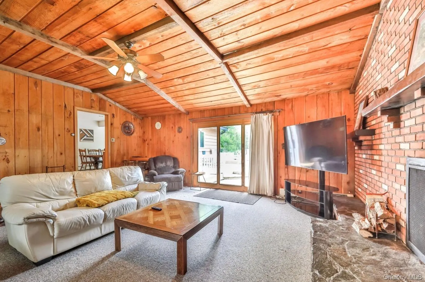 Carpeted living room with wood ceiling, ceiling fan, wooden walls, and a fireplace Carpeted living room with wood ceiling, ceiling fan, wooden walls, and a fireplace