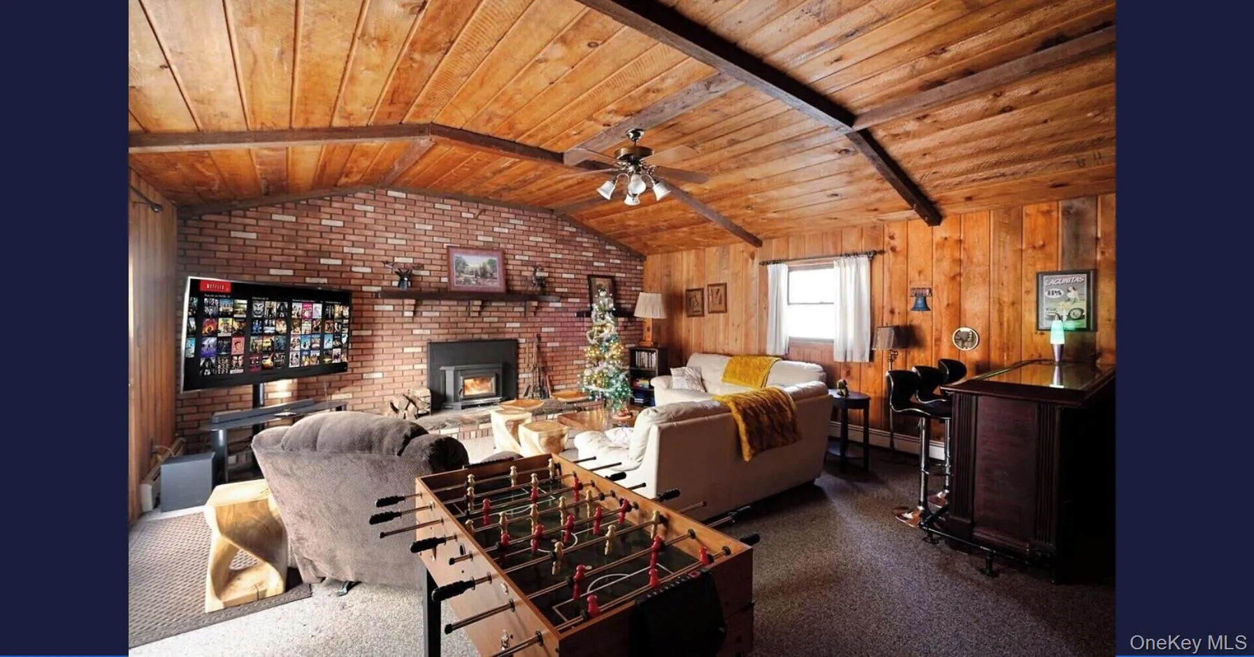 Living area featuring wood ceiling, a ceiling fan, brick wall, wooden walls, and a fireplace Living area featuring wood ceiling, a ceiling fan, brick wall, wooden walls, and a fireplace