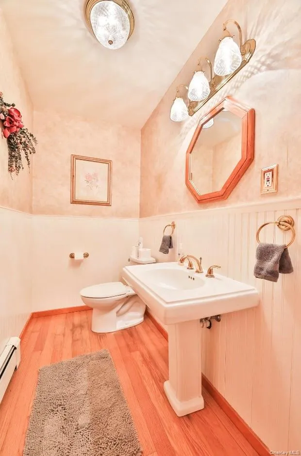 Half bath featuring a wainscoted wall, light wood-type flooring, and a baseboard heating unit Half bath featuring a wainscoted wall, light wood-type flooring, and a baseboard heating unit