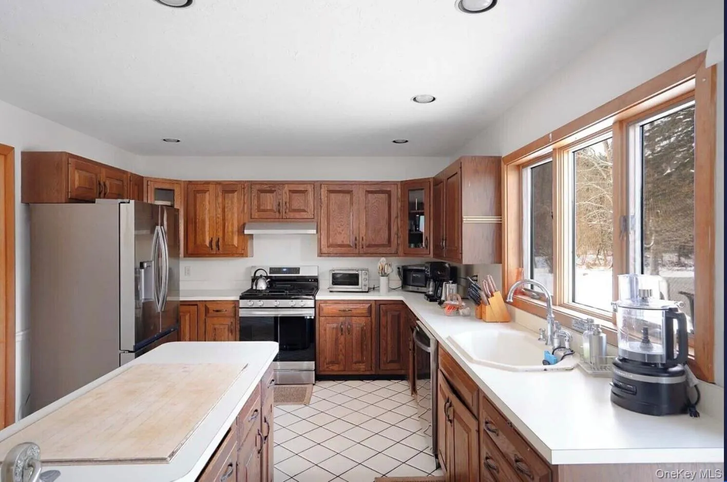 Kitchen featuring stainless steel appliances, brown cabinetry, light countertops, light tile patterned floors, and recessed lighting Kitchen featuring stainless steel appliances, brown cabinetry, light countertops, light tile patterned floors, and recessed lighting