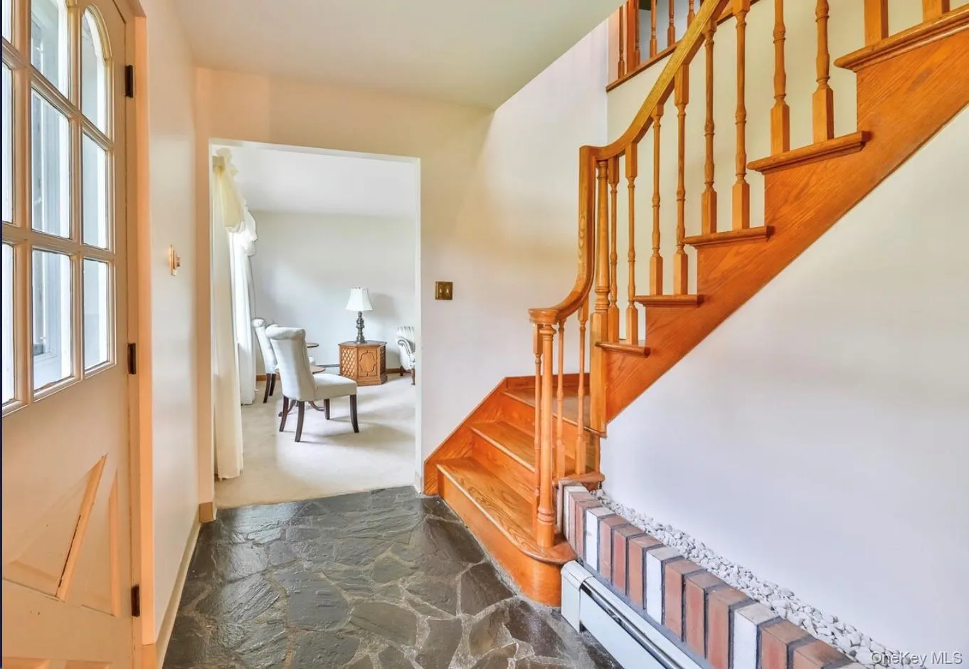 Foyer with a baseboard radiator, dark stone finish flooring, dark carpet, and stairs Foyer with a baseboard radiator, dark stone finish flooring, dark carpet, and stairs