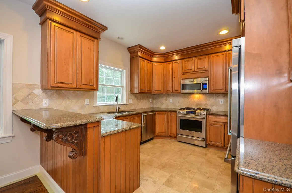 Kitchen with brown cabinetry, light stone countertops, appliances with stainless steel finishes, a peninsula, and recessed lighting Kitchen with brown cabinetry, light stone countertops, appliances with stainless steel finishes, a peninsula, and recessed lighting