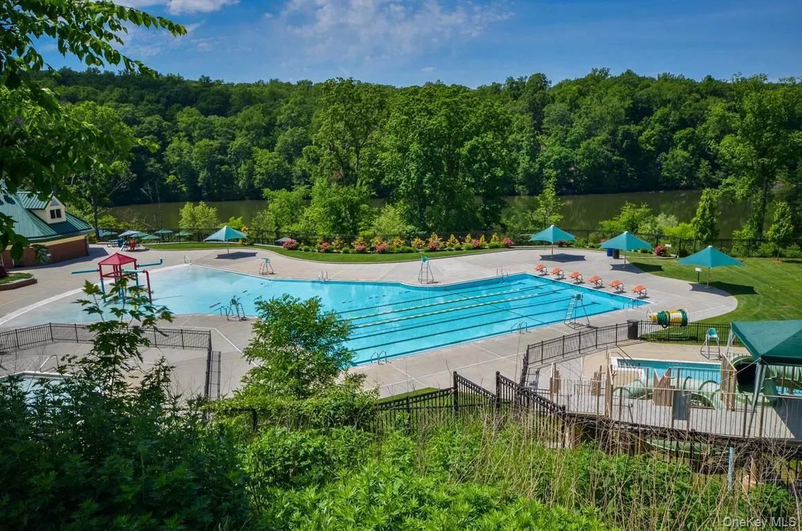 Community pool with a patio area, a water view, and view of wooded area Community pool with a patio area, a water view, and view of wooded area