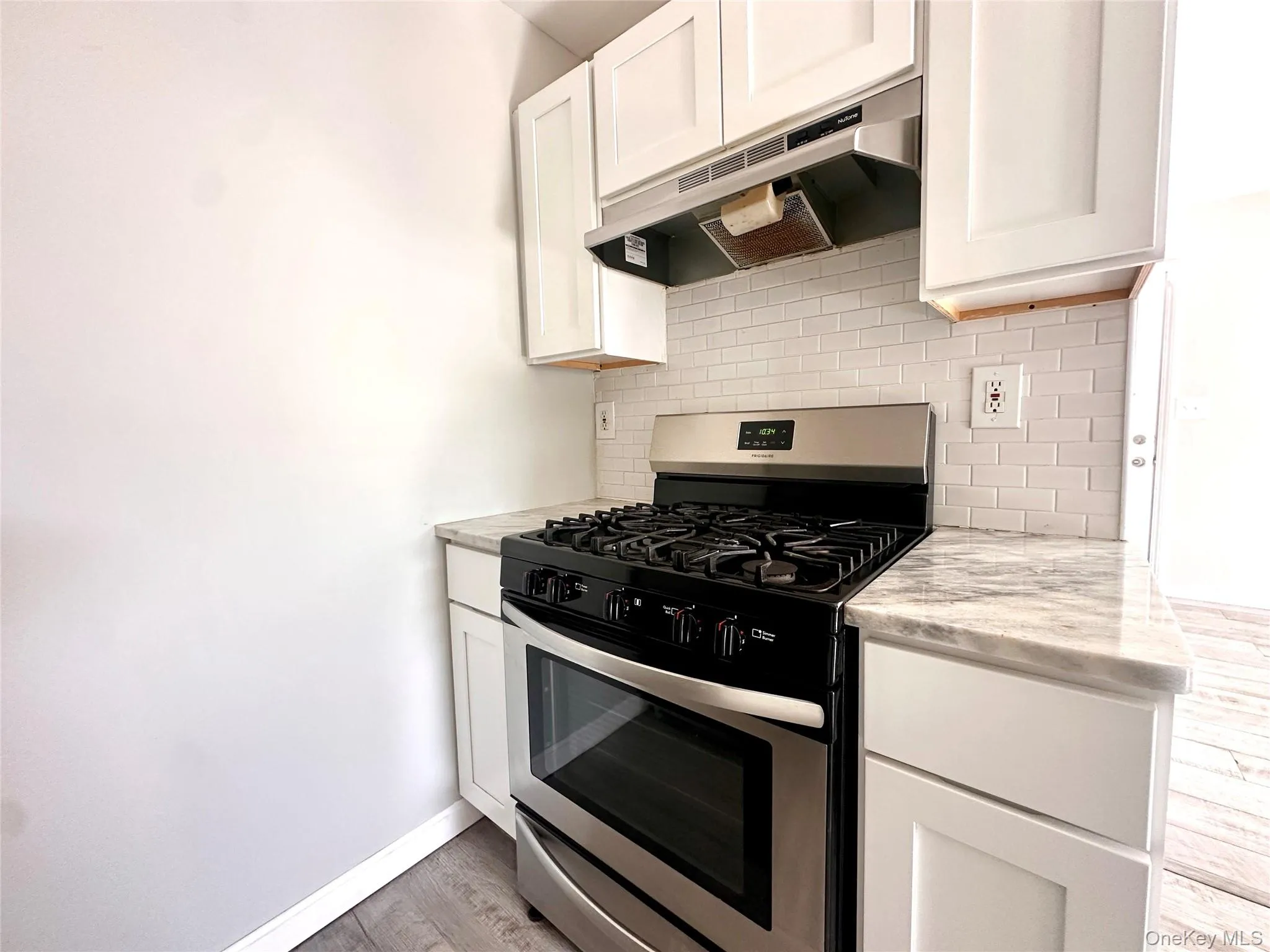 Kitchen featuring stainless steel gas range oven, under cabinet range hood, white cabinetry, and decorative backsplash Kitchen featuring stainless steel gas range oven, under cabinet range hood, white cabinetry, and decorative backsplash