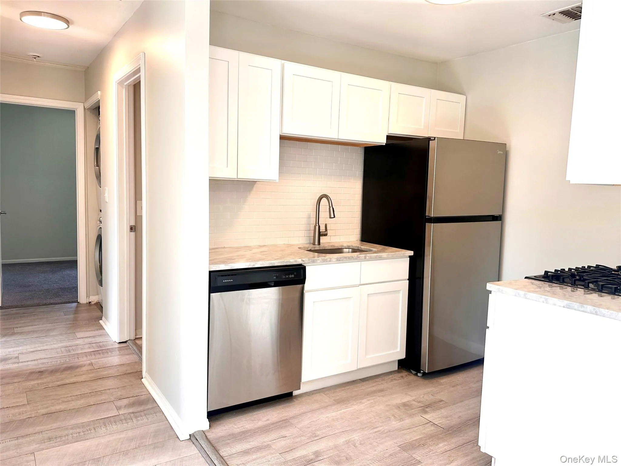 Kitchen with decorative backsplash, stainless steel appliances, white cabinetry, and light wood-type flooring Kitchen with decorative backsplash, stainless steel appliances, white cabinetry, and light wood-type flooring