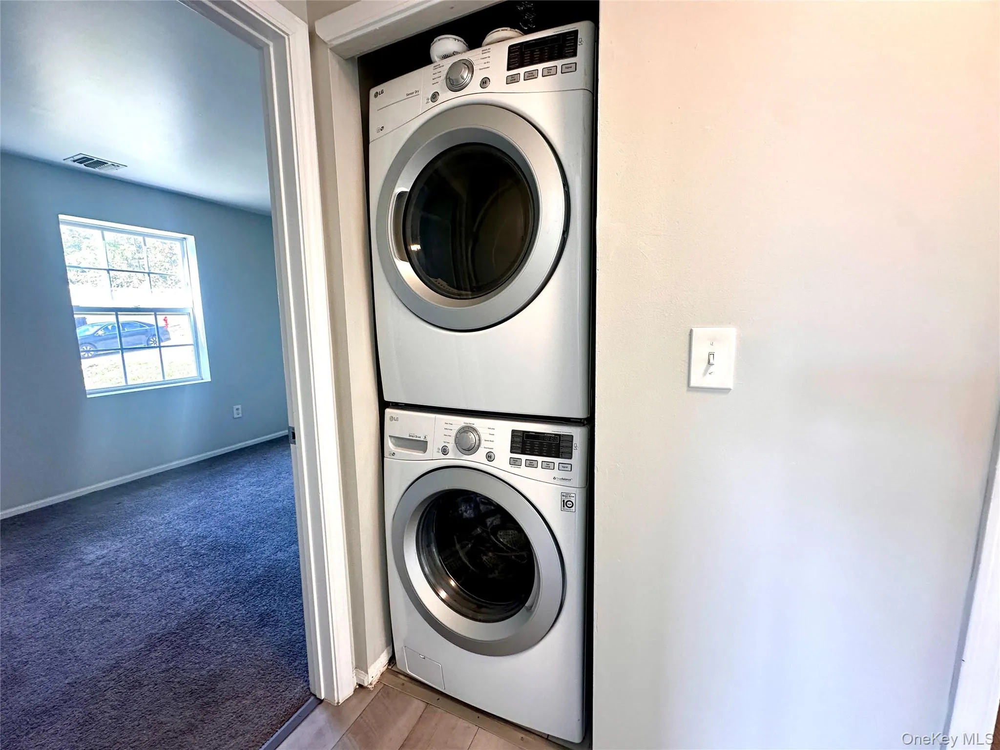 Washroom featuring stacked washing machine and dryer and dark carpet Washroom featuring stacked washing machine and dryer and dark carpet
