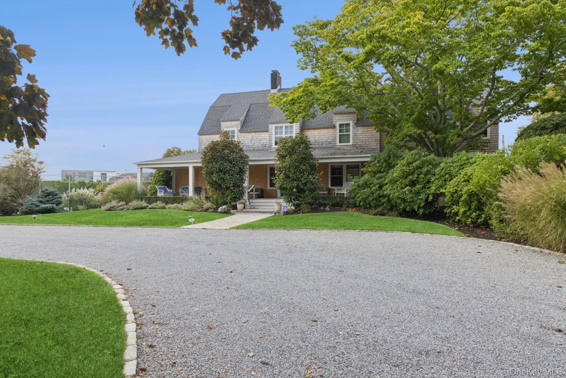 Shingle-style home featuring a porch, a gambrel roof, a front yard, and a chimney Shingle-style home featuring a porch, a gambrel roof, a front yard, and a chimney